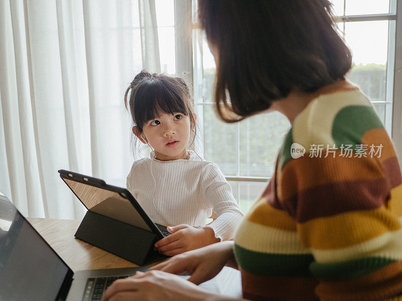 年轻母亲在家工作，女儿在餐桌上。