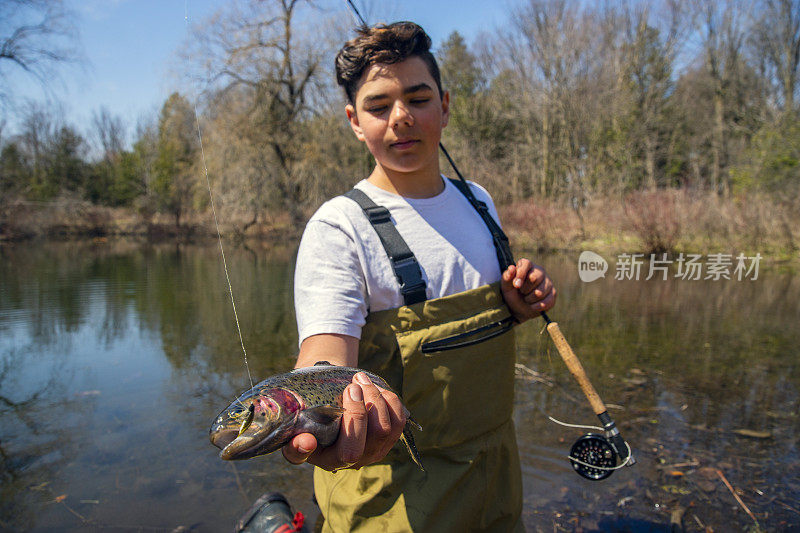 一个十几岁的飞钓少年拿着刚钓到的虹鳟鱼。