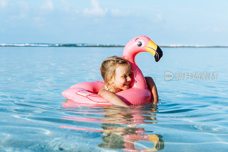 可爱的金发小女孩和粉红色的充气火烈鸟游泳在热带海洋的暑假。
