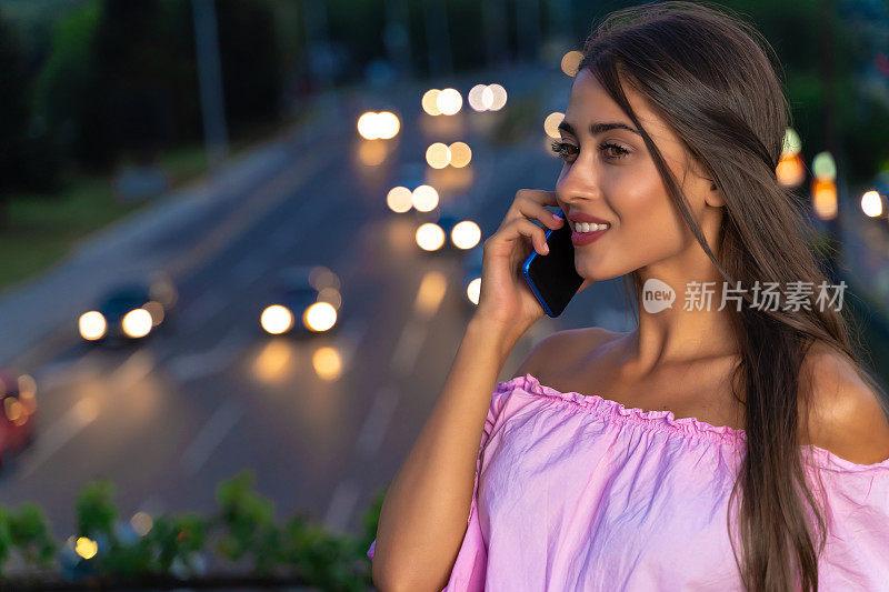 年轻美丽的女孩使用她的智能手机在繁忙的城市街道晚上