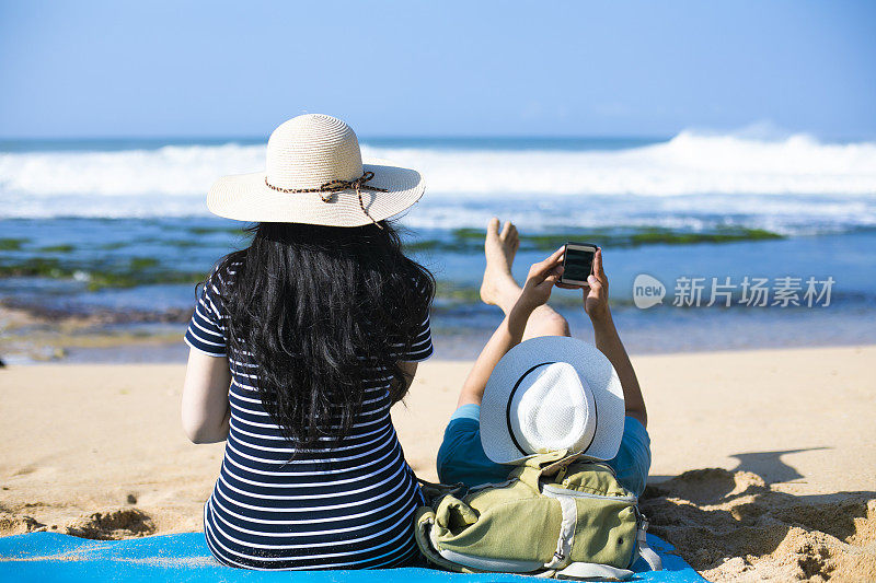一对亚洲年轻夫妇坐在海滩上遥望远方
