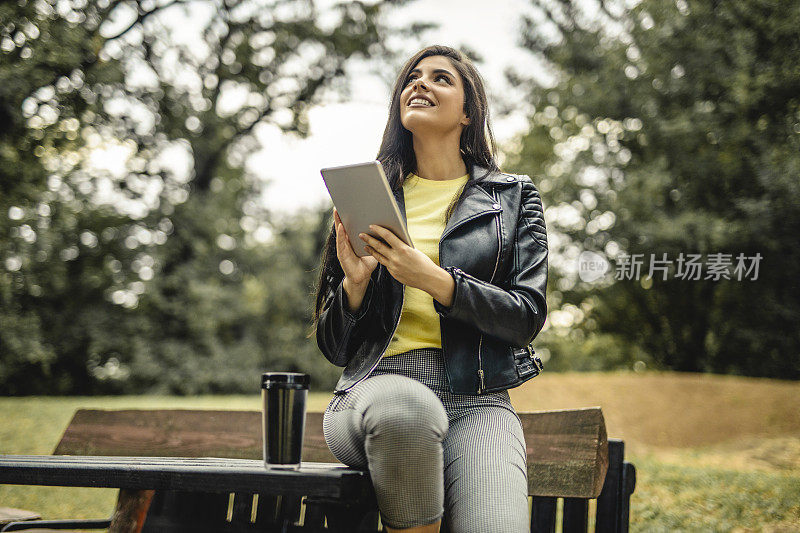年轻漂亮的女人在户外喝咖啡，在平板电脑上读电子书