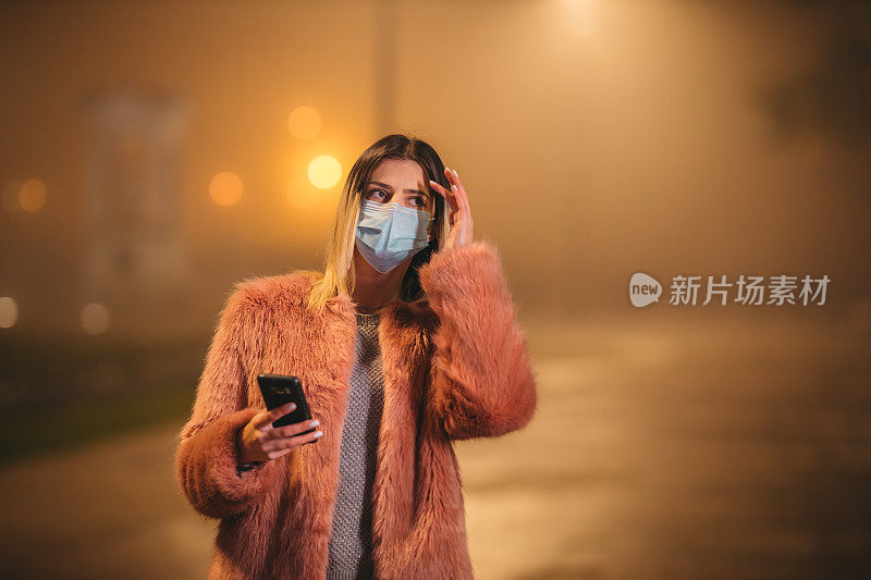 一个戴着口罩的女人走在人行道上打电话。被污染的空气。