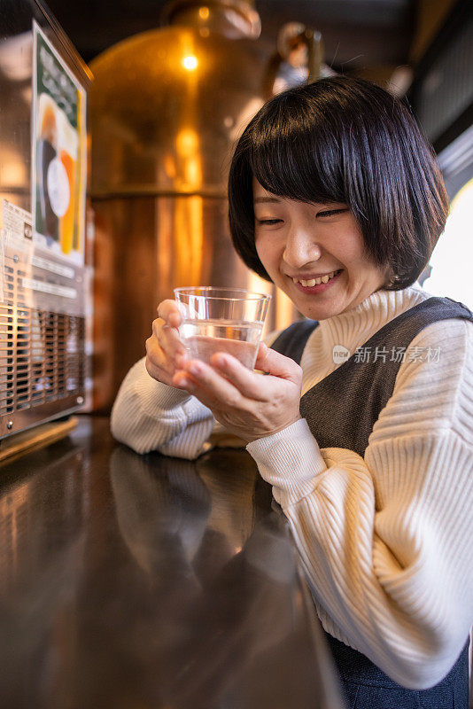 在传统的日本温泉区，快乐的年轻女子拿着一杯“saki”(日本米酒)