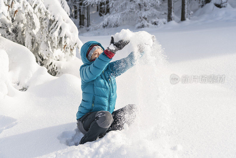 在冬天的森林里，成熟的女人穿着皮大衣向空中抛雪