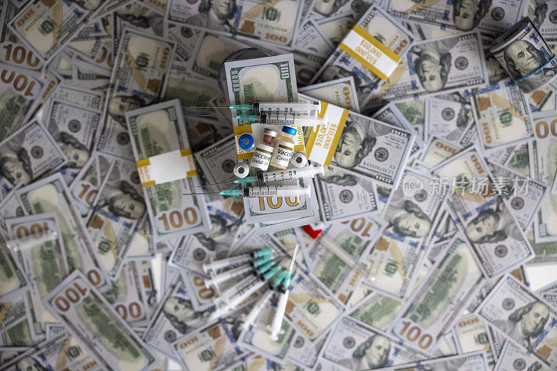新冠肺炎疫苗放在一堆100美元钞票上，旁边是注射器