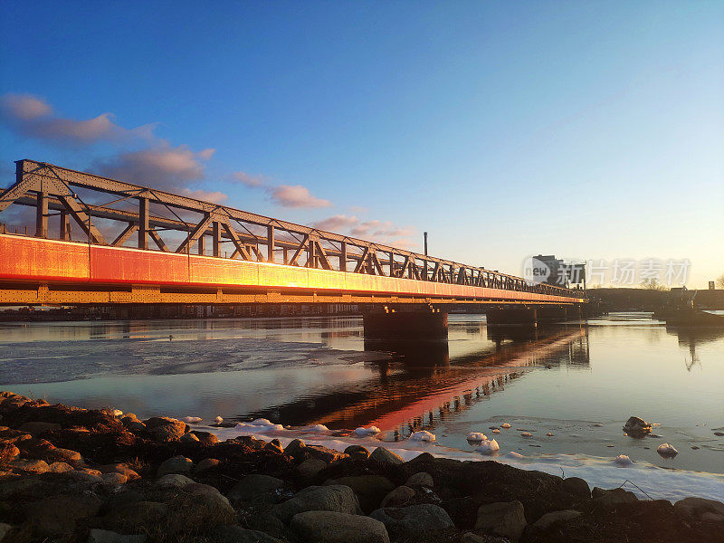 丹麦日落时冰冻的水面上的红色人行天桥