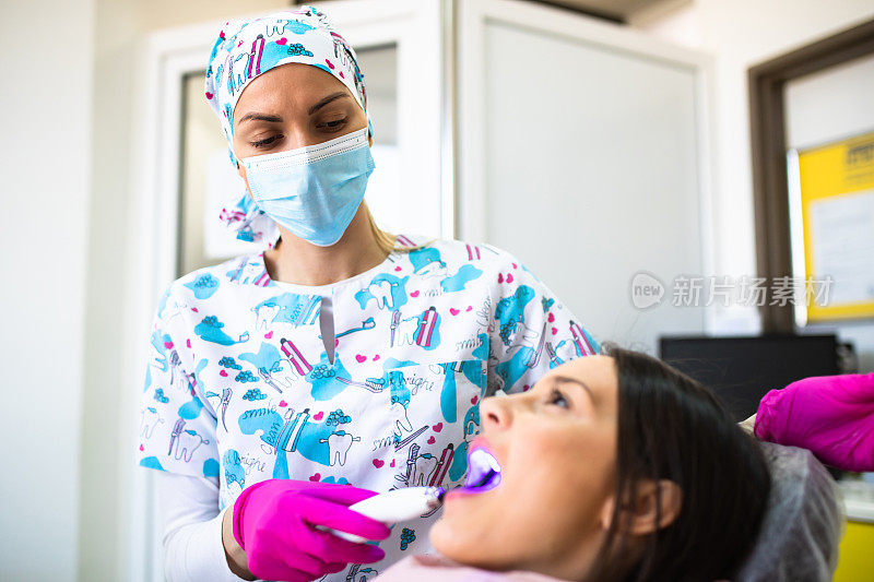 一个女牙医用蓝光聚合一个年轻女性的填充物