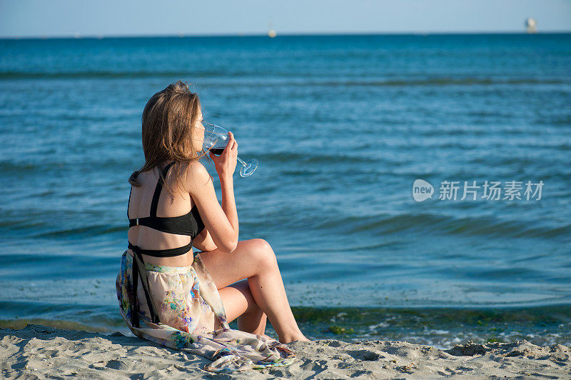 年轻女子坐在海滩上，手里拿着酒杯