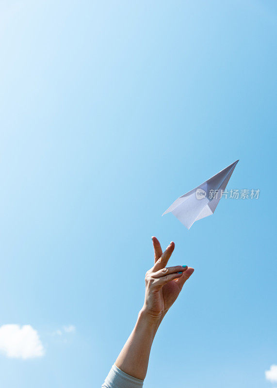 女子手扔纸飞机在蓝天上