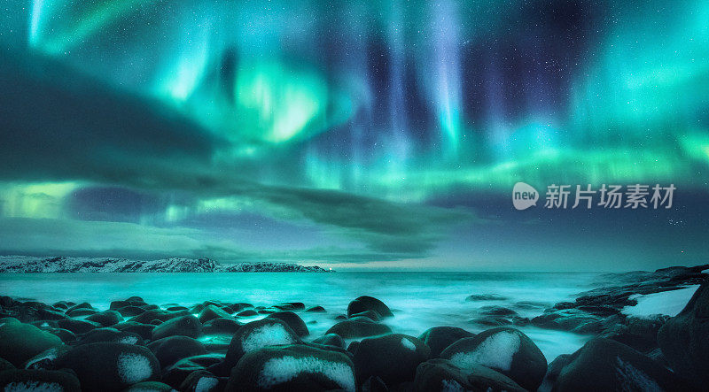 北极光。俄罗斯捷里别尔卡海面上的北极光。星空，极地的光和云。夜晚冬天的景观与明亮的极光，星星，大海，雪石在模糊的水。旅行