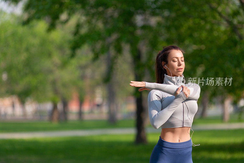 女人在跑步或锻炼前伸展肩膀来热身。健康的生活方式的概念
