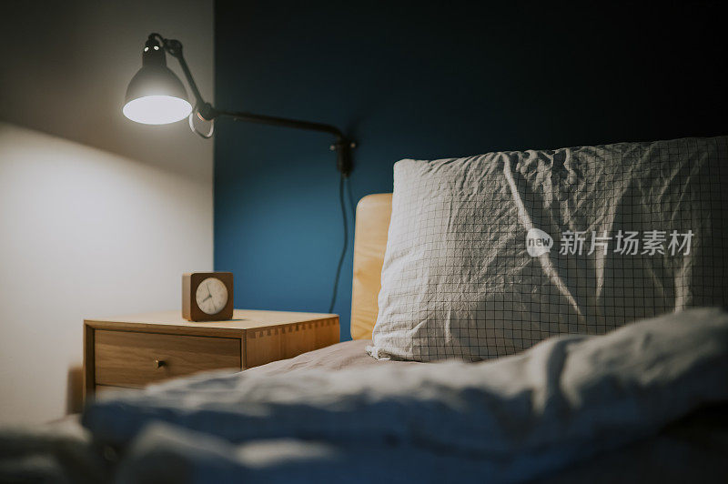 卧室在晚上由电灯和时钟照亮床头柜旁边的床与蓝色墙壁