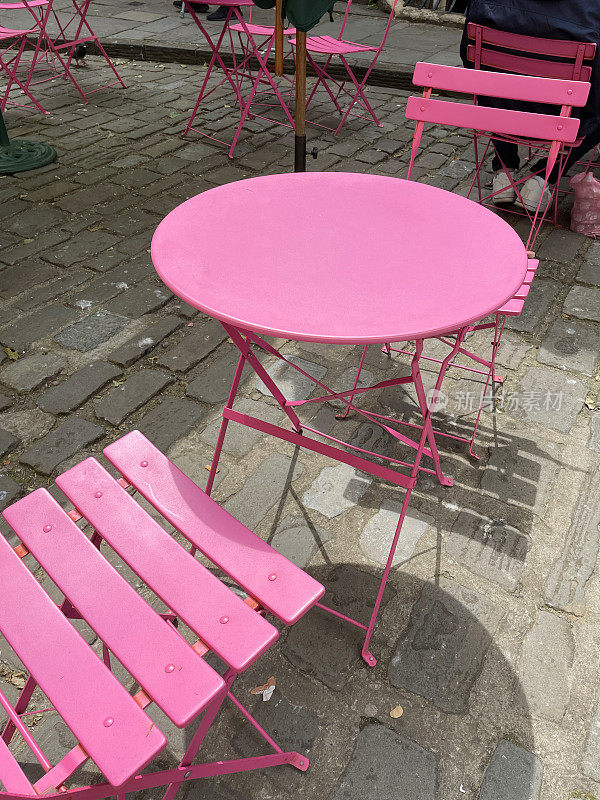 彩色的图像，圆形的金属庭院庭院桌椅漆成亮粉色，在鹅卵石街道上的露天餐厅
