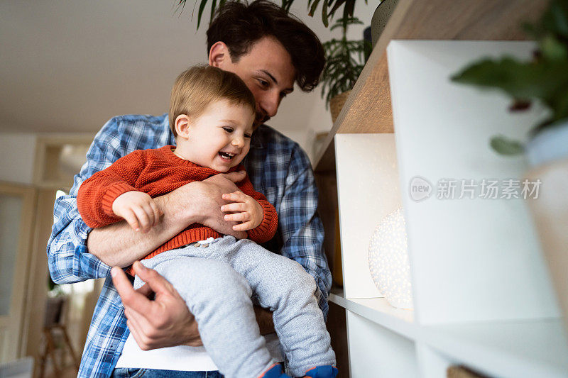 年轻的白人父亲抱着他的婴儿儿子，他正在玩架子上的灯