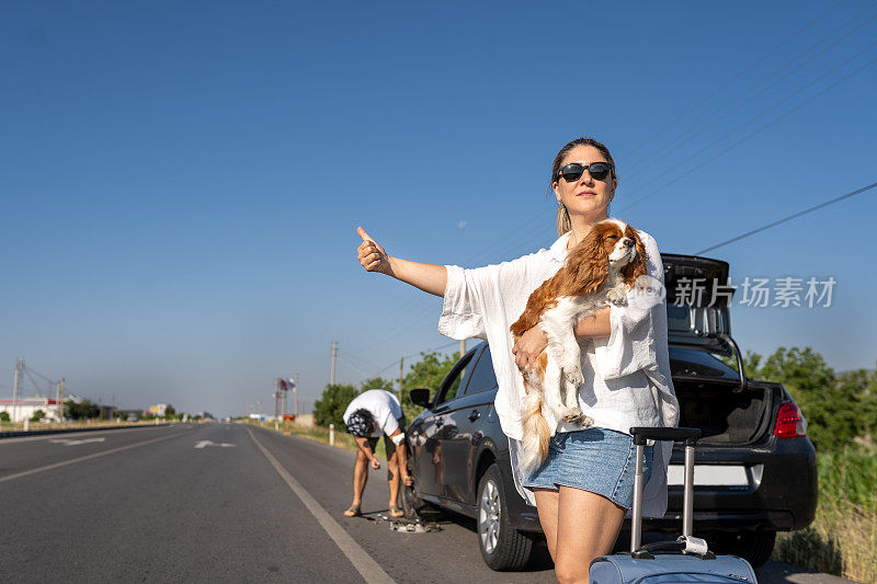 一名年轻女子带着她的狗搭车时，一辆轮胎漏气的汽车正在路上修理