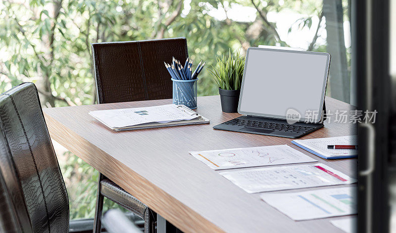 模拟空白屏幕便携式平板电脑魔法键盘和文件在会议室的木桌。