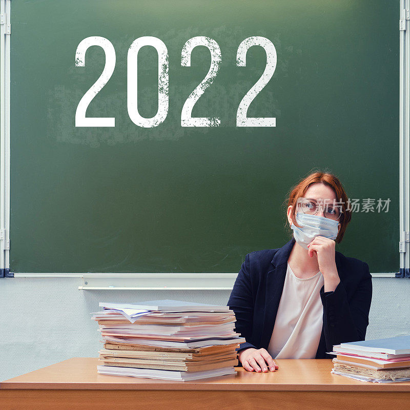女老师在课堂上用粉笔在黑板上题字2022。新学年的冠状病毒问题，复制空间