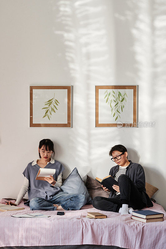 集中注意力的亚洲学生在考试前坐在床上阅读书本和练习册