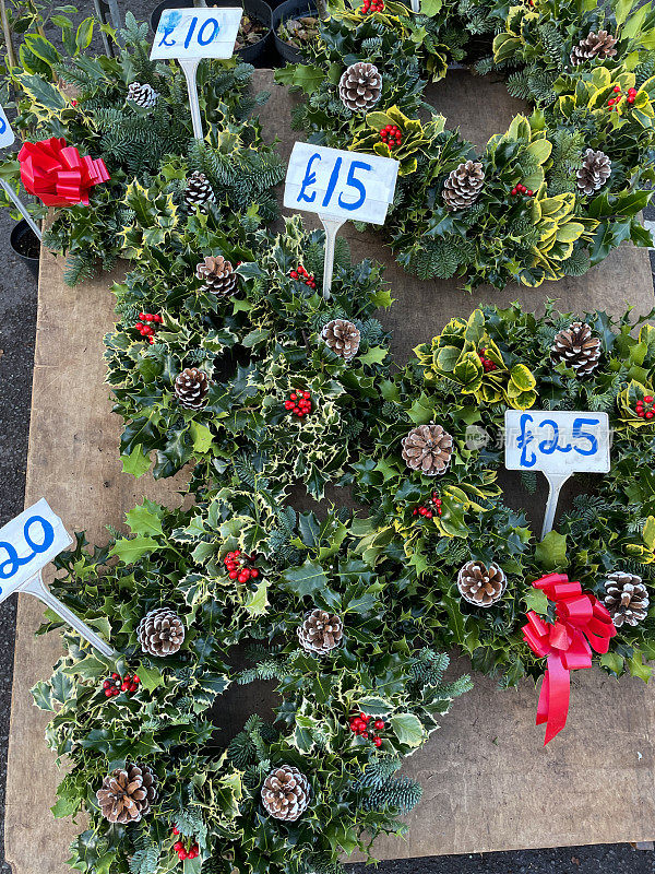 市场摊位展示的圣诞花环胶合板的图片，价格标签，花环由云杉，冬青和松果，红色蝴蝶结和浆果制成，高架视野