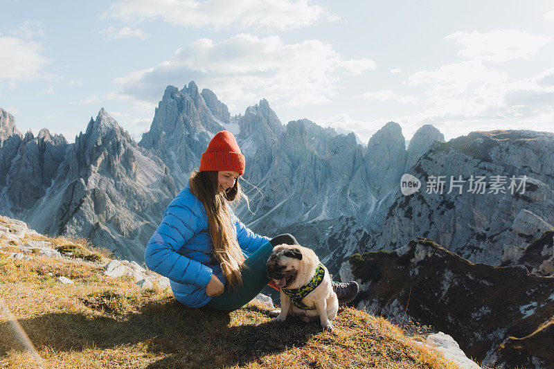 微笑的女人和她的狗凝视着风景优美的山脉，在Dolomites阿尔卑斯山的草地上放松