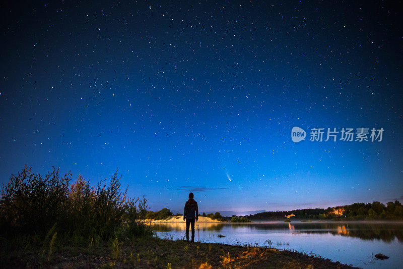 星空背景下的男人轮廓。夜空中的彗星。夏天的星空。美丽的风景伴着星星。长时间的曝光。关于水资源的雾。大气的格局。晨光。