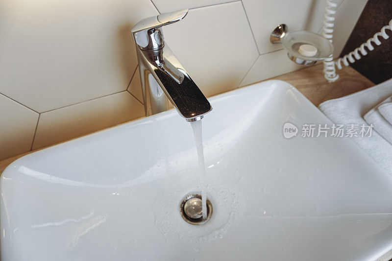 从水龙头流出的水流过水槽。这是一个特写镜头，水从浴室里的面盆龙头里流出。浴室里的陶瓷脸盆，有一个龙头，水从里面流出来。
