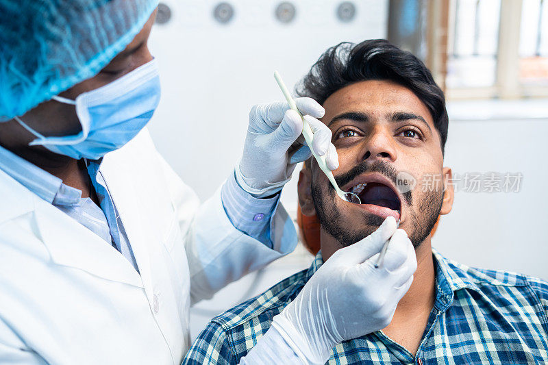 戴着外科手套的牙医在医院或诊所检查病人牙齿的特写——口腔护理的概念，治疗牙痛和专业的职业。