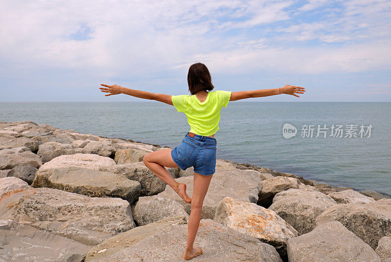 苗条的女孩在海边堤岸的岩石上一边做体操一边用一条腿保持平衡