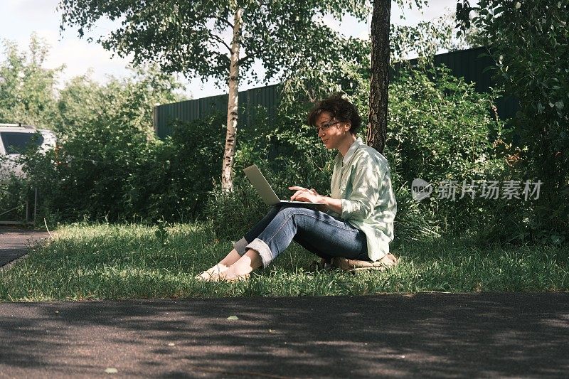 成熟的女人是坐在草地上使用笔记本电脑