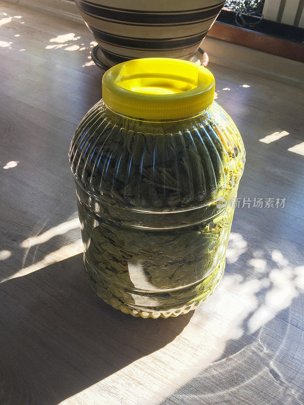 葡萄叶装在透明的塑料瓶里，腌制好的葡萄叶放在厨房地板上