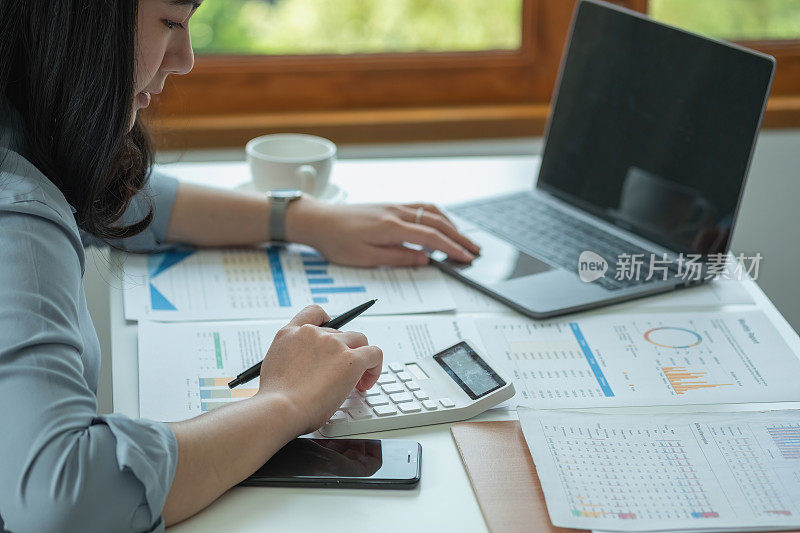 商务女性手持笔，通过笔记本电脑向主管展示图表形式的利润数据。