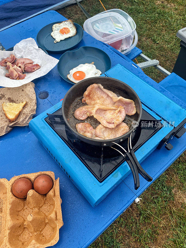 露营在户外吃英式早餐。在野营桌上的煤气炉上做饭。