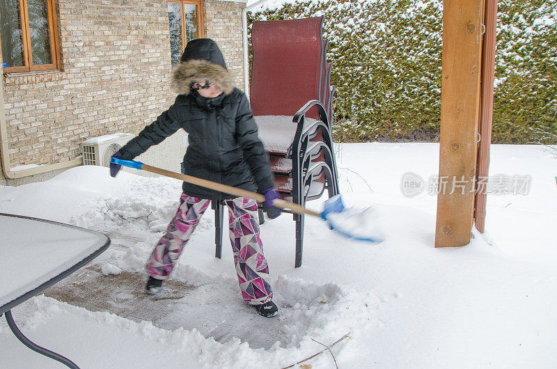 一个十几岁的女孩在室外露台上铲雪