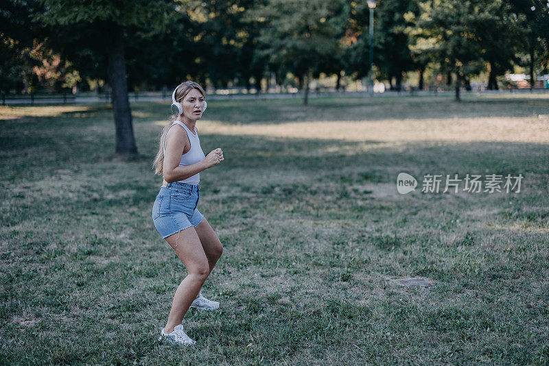 一名年轻女子边听音乐边伸展身体，准备在大自然中进行训练。