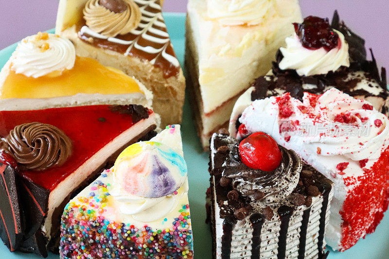 粉彩蓝色盘子上各种蛋糕切片的全帧图像，天使食物蛋糕，巧克力和樱桃蛋糕，黑森林蛋糕，红天鹅绒蛋糕，彩虹蛋糕，咖啡和大理石巧克力蛋糕，盐焦糖蛋糕，紫色背景