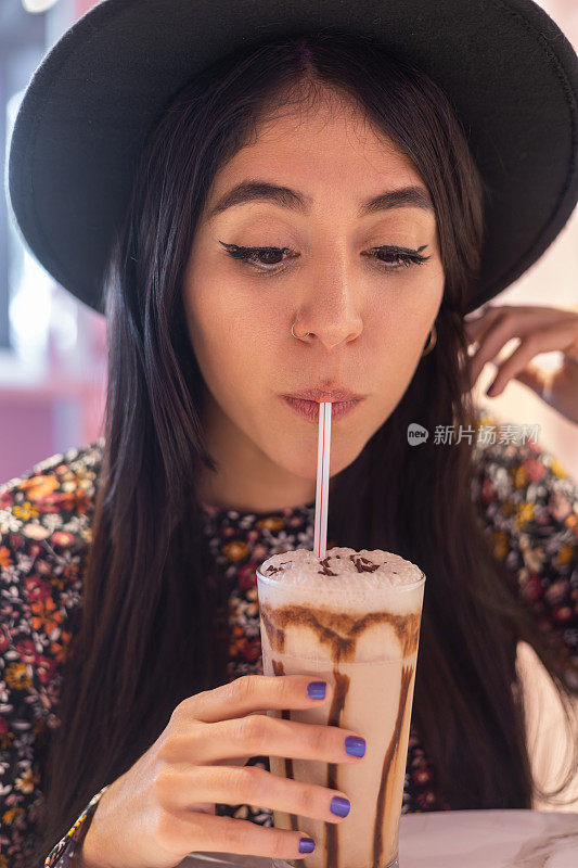 一个戴着帽子的年轻女子用吸管喝着咖啡，喝着爽口的饮料