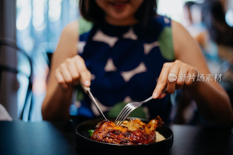 一位亚洲女性在餐厅享用烤鸡腿的特写镜头