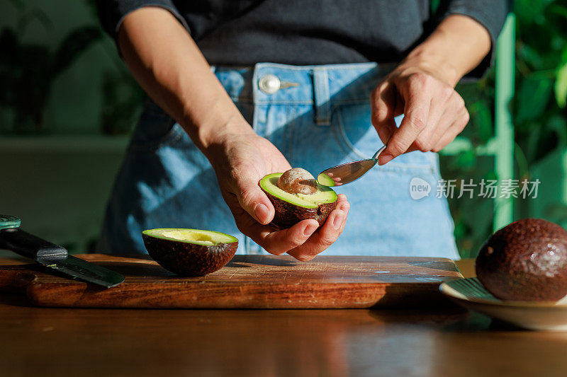 这是一张特写照片，一个女人在砧板上熟练地用勺子剥牛油果，美丽的早晨阳光照在牛油果上。