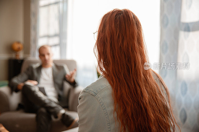 一个年轻的白人妇女与红头发是在一个治疗会议与男性心理学家，在咨询会议期间参与讨论