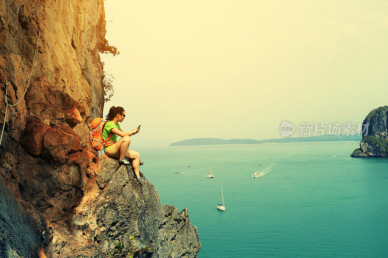 一名年轻的攀岩者在海边的悬崖边使用智能手机