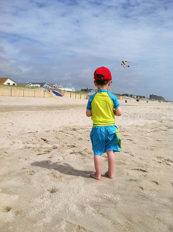 光着脚蹒跚学步的小男孩在海滩上放着他的条纹风筝。