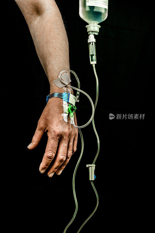 静脉输液患者的手和手臂，黑色背景，垂直。