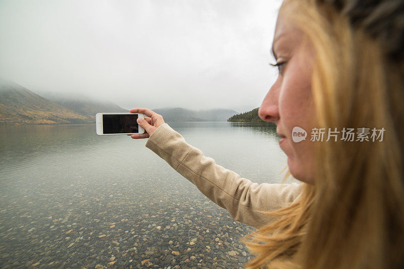 一名女子在湖边用手机拍摄风景