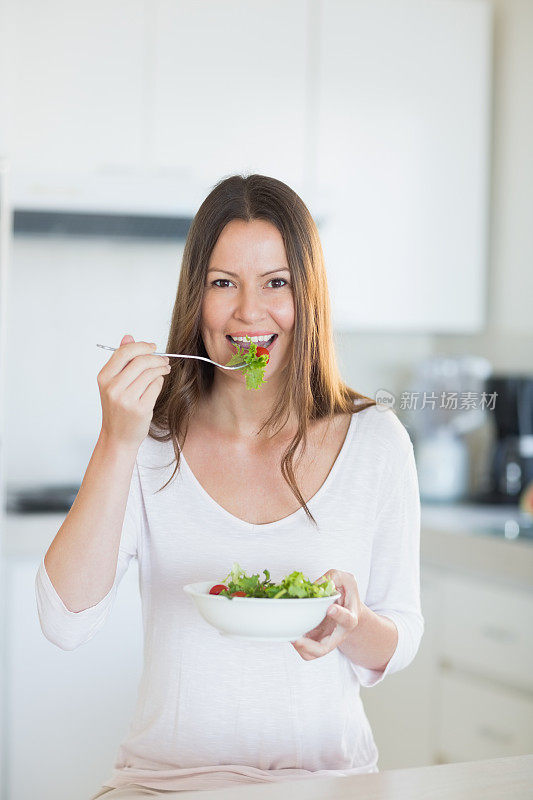 微笑的年轻女子在厨房里拿着一碗沙拉