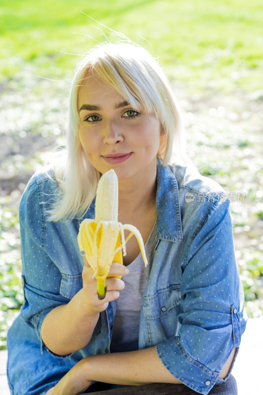 迷人的女人吃香蕉，自然的绿色春天的背景