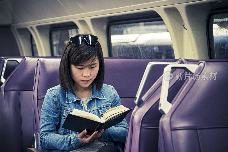 年轻的亚洲女学生在火车车厢里阅读课本