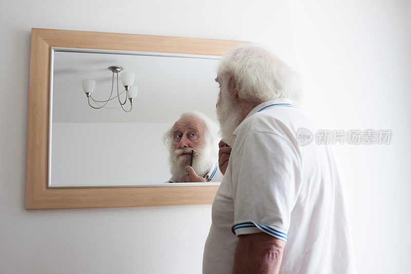 年长的大胡子男人在镜子里梳理小胡子