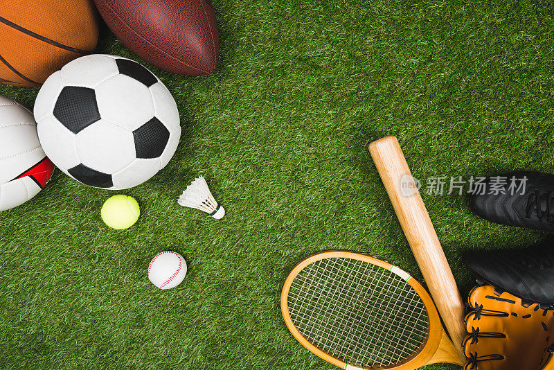 俯视图各种运动球，棒球拍和手套，羽毛球拍在绿色草坪上