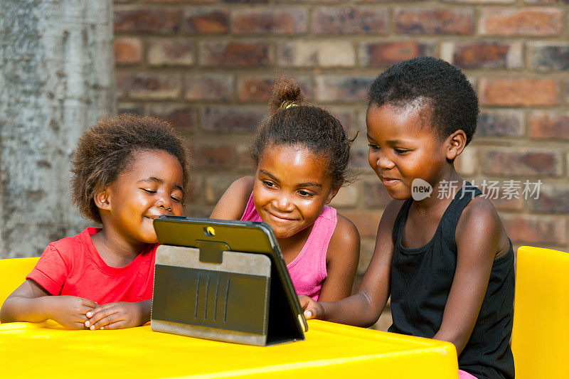 三个非洲小孩一起玩平板电脑。